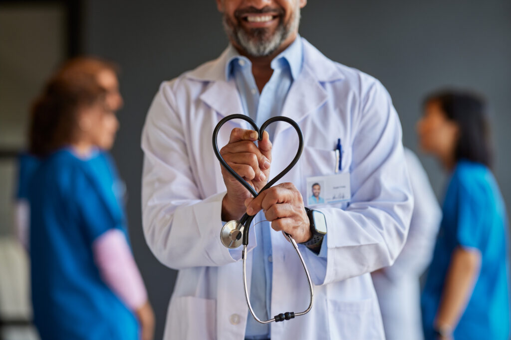 Smiling doctor holding heart shape stethoscope at hospital