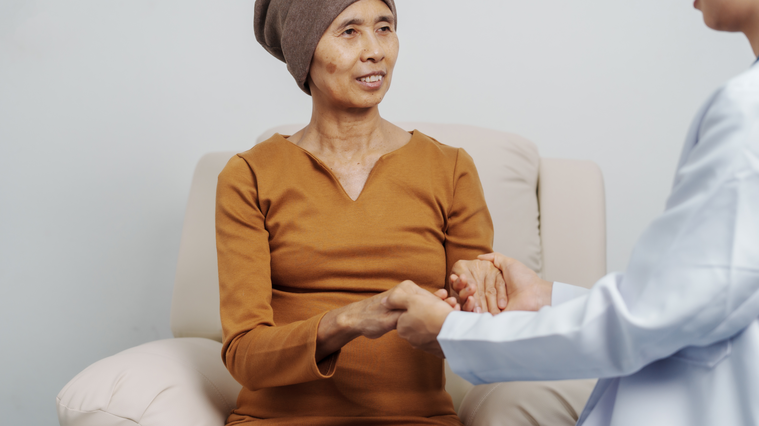 Doctor offering emotional support to a cancer patient wearing a headscarf during a cancer treatment consultation.