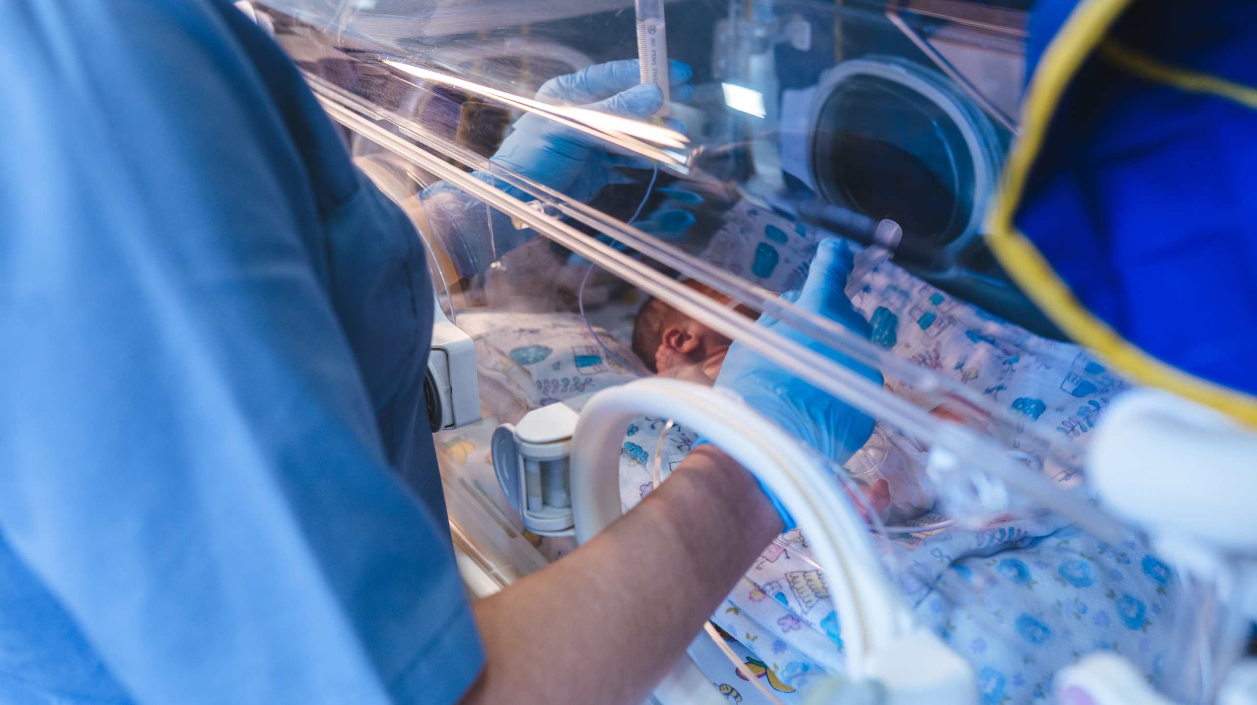 Neonatal intensive care unit (NICU) staff caring for a premature newborn inside an incubator with advanced medical support equipment.