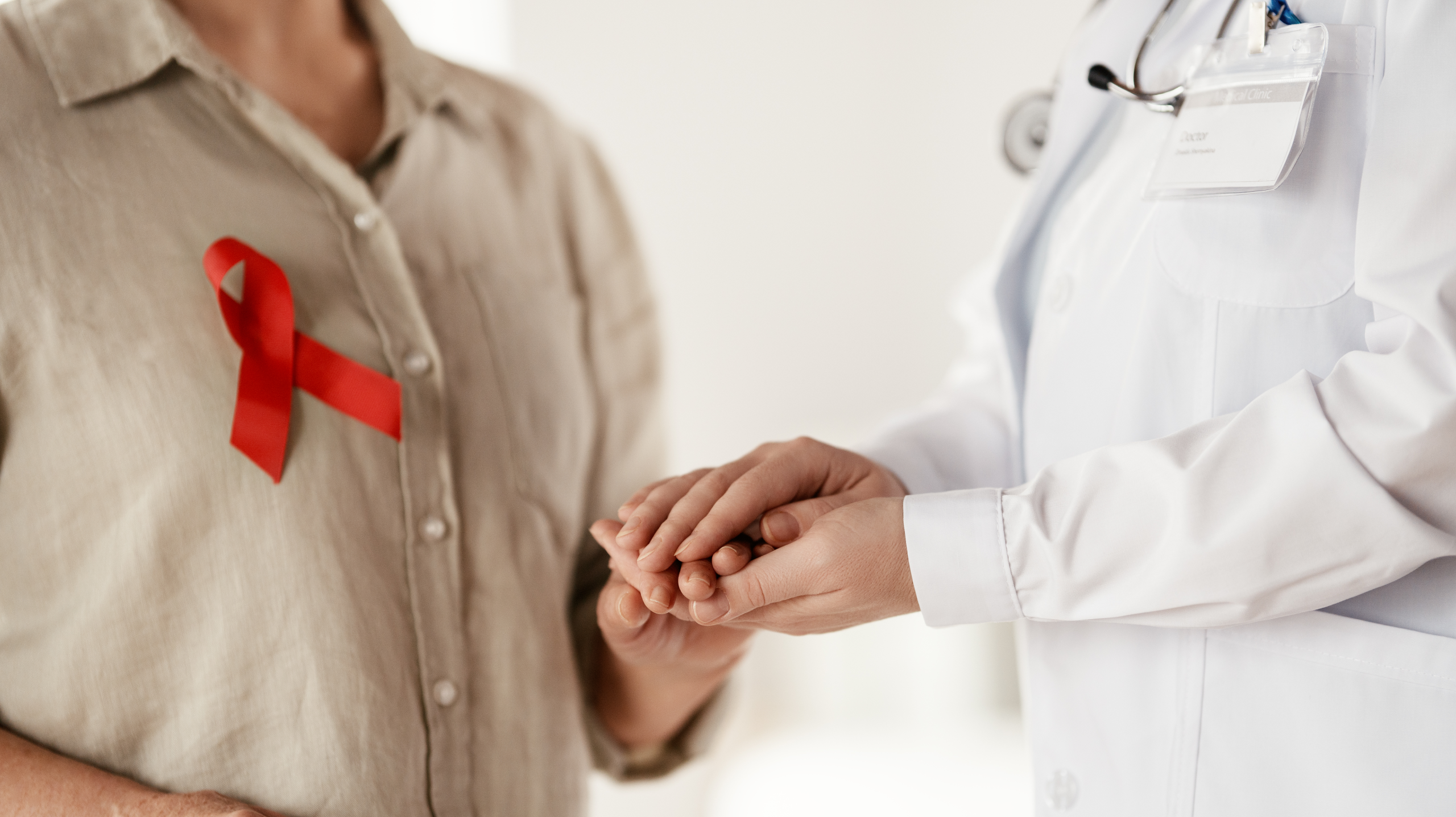 Doctor supporting a cancer patient wearing a red awareness ribbon during a cancer treatment consultation.