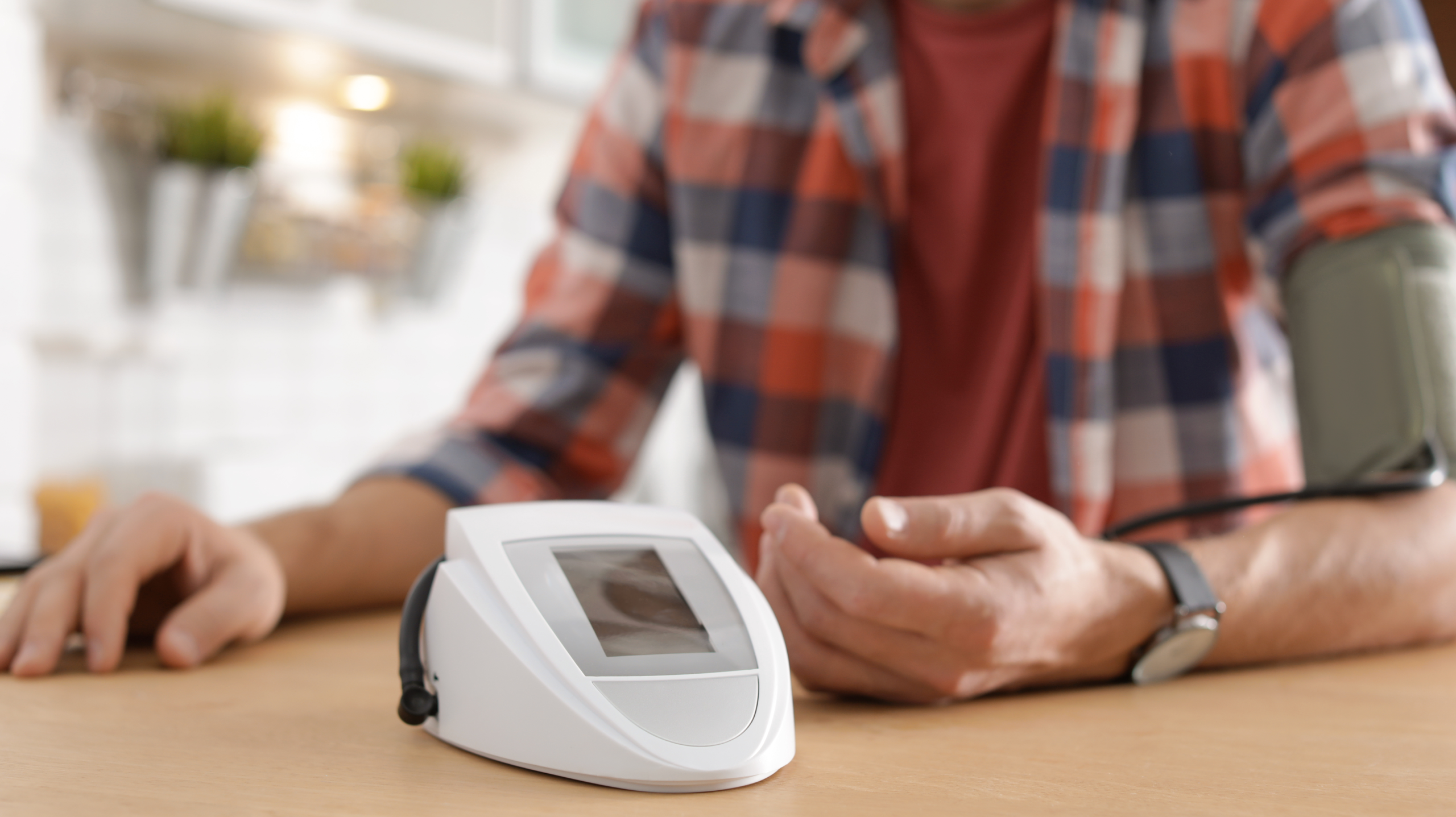 Person checking blood pressure at home using a digital monitor while sitting at a table.
